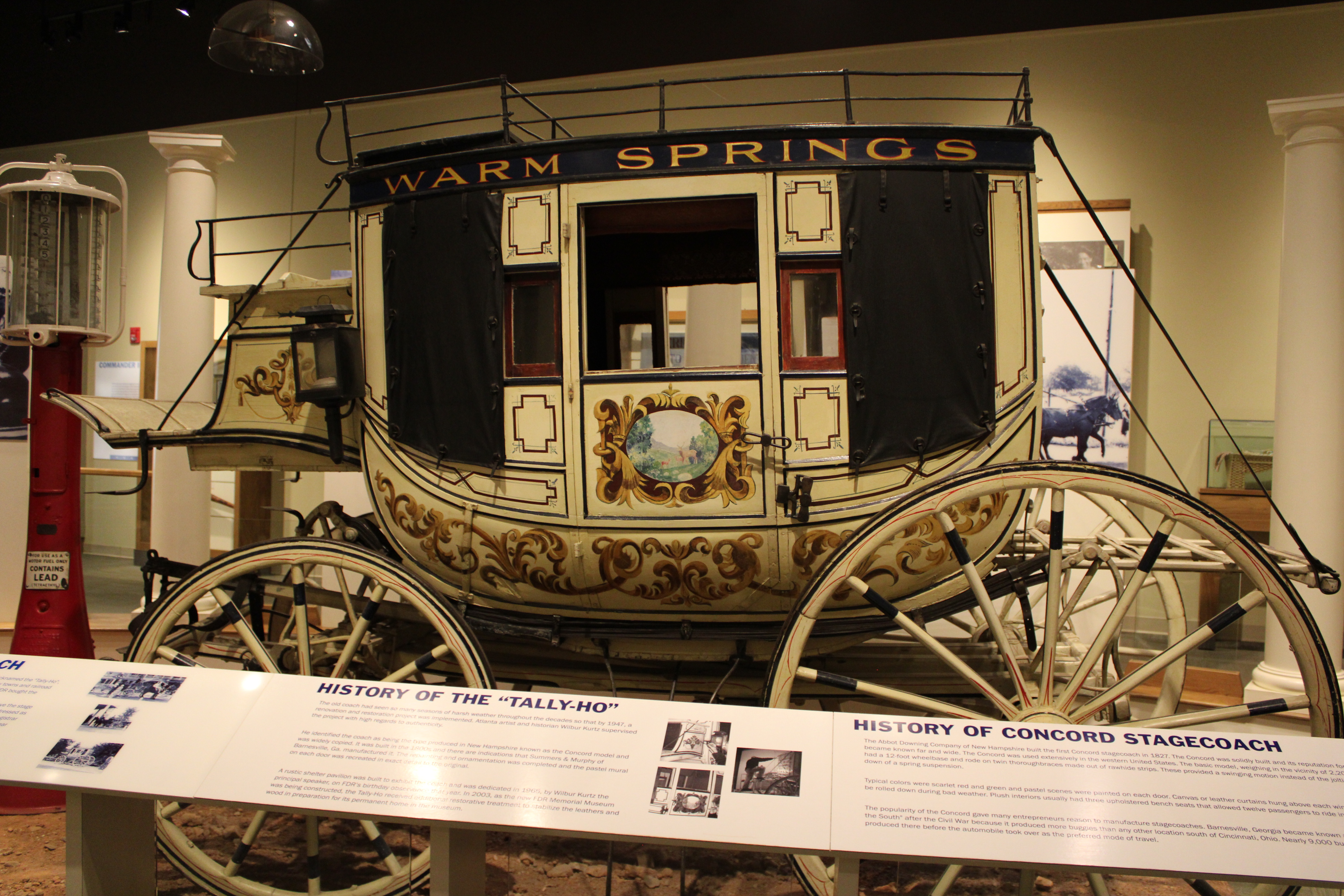 A beige stagecoach with ornamental decoration throughout. Near the top the words WARM SPRINGS are painted.